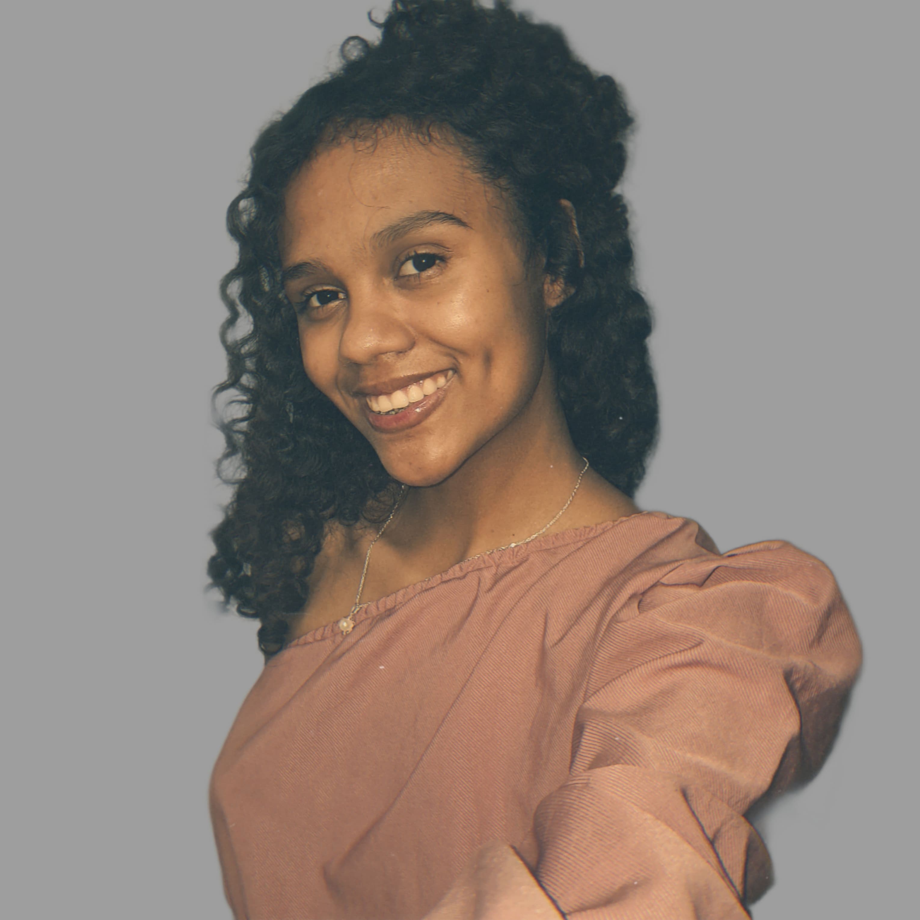 Foto da integrante Emily Amorim, ela está usando uma roupa rosa, tem cabelo cacheado;